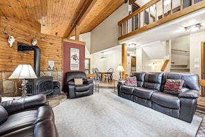 Ein großzügiger Wohnraum mit Kamin, Ledersofas und einer hohen Decke mit Holzbalken.