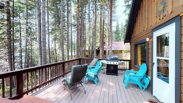 A wooden deck with outdoor seating and a grill, surrounded by tall trees.