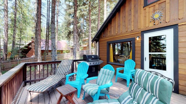 Eine Holzterrasse mit Grill, Streifenstuhle und einer Couch.