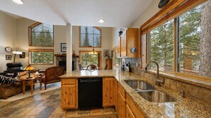 A spacious kitchen with granite countertops, wooden cabinets, and a large window offering a view of trees. - McCall Golf Course Cabin | Pool, Deck, Loft (McCall)