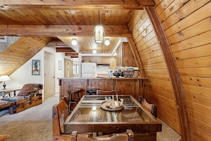 A cozy wooden interior with a dining area, kitchen, and a loft bedroom. - Downtown McCall A-Frame Cabin | Walk to Lake (McCall)