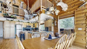 Une cabane en bois spacieuse comprenant un coin repas central, une cuisine et une chambre à coucher située en mezzanine.