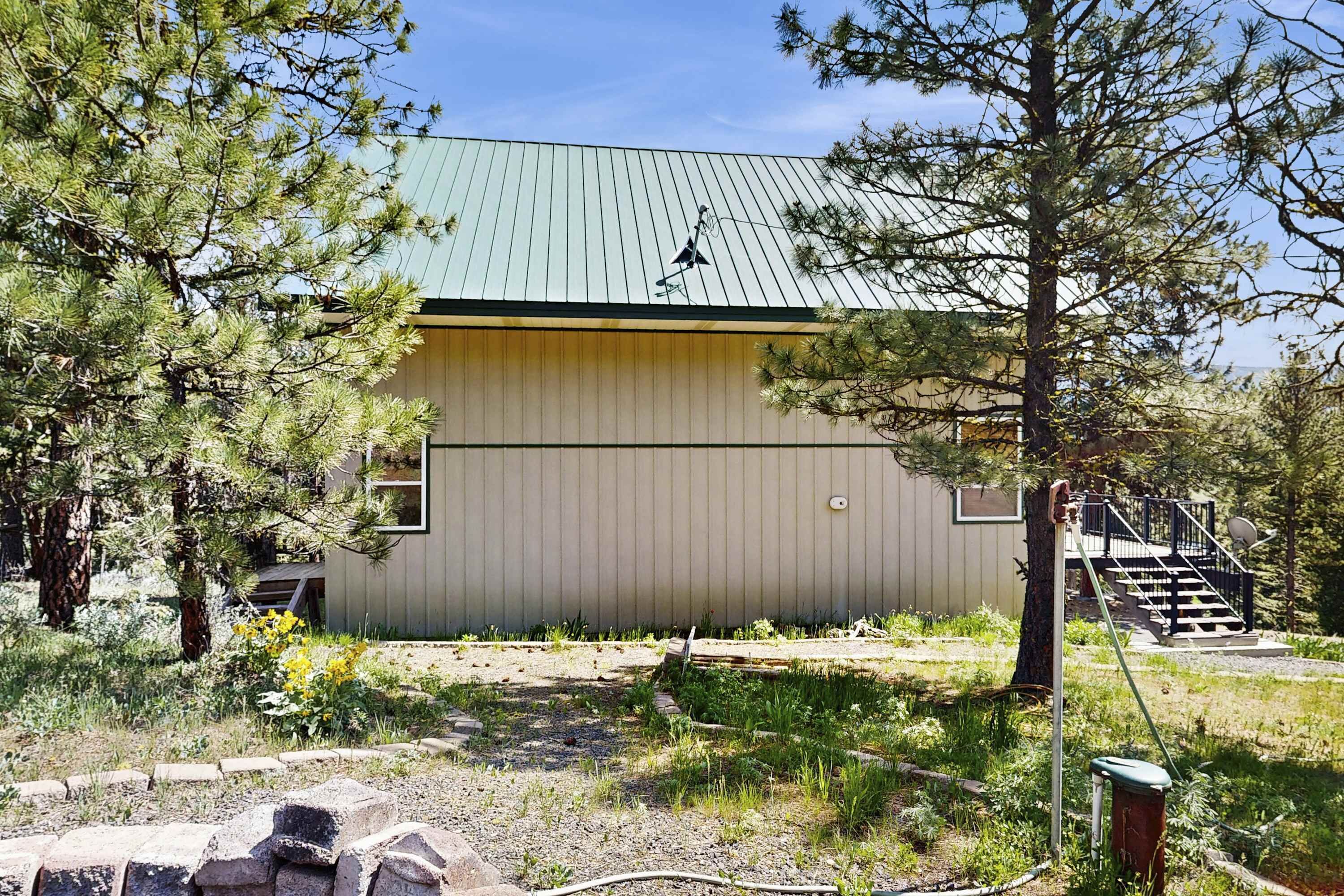 A building with a metal roof, surrounded by trees and a garden area.