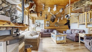 L’intérieur d’un chalet rustique, avec un plancher en bois, un mur en pierre et divers trophées d’animaux fixés aux murs.