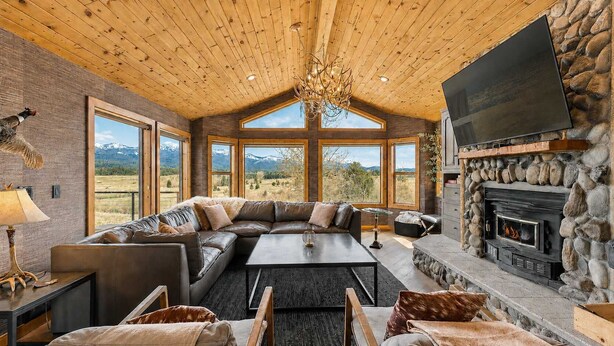 A cozy interior with a stone fireplace, leather sofa, and large windows offering mountain views. - Luxury Mountain View Retreat | Hot Tub & Game Room (McCall)