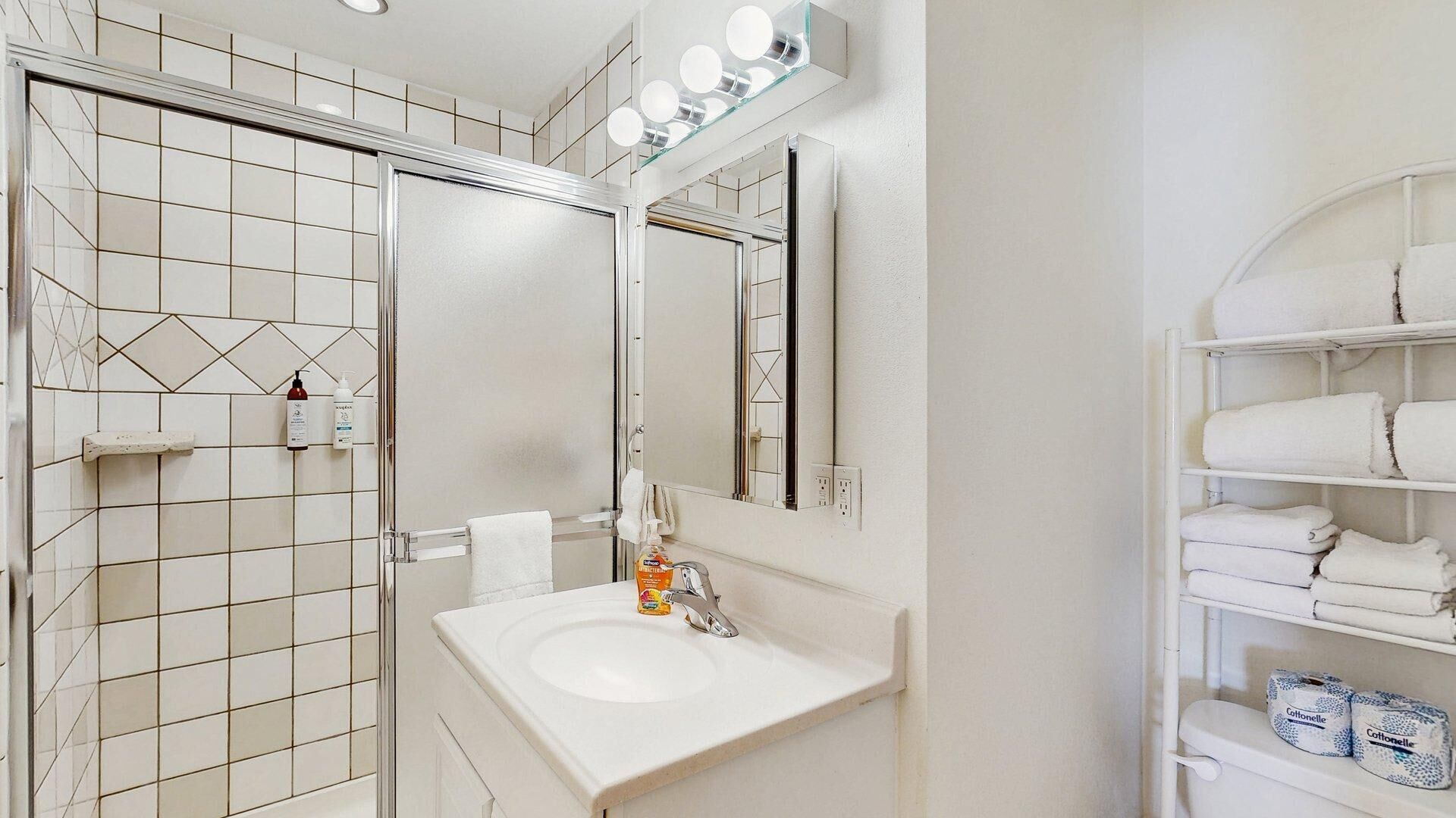 A bathroom with a white sink, mirror, and shelves with towels.
