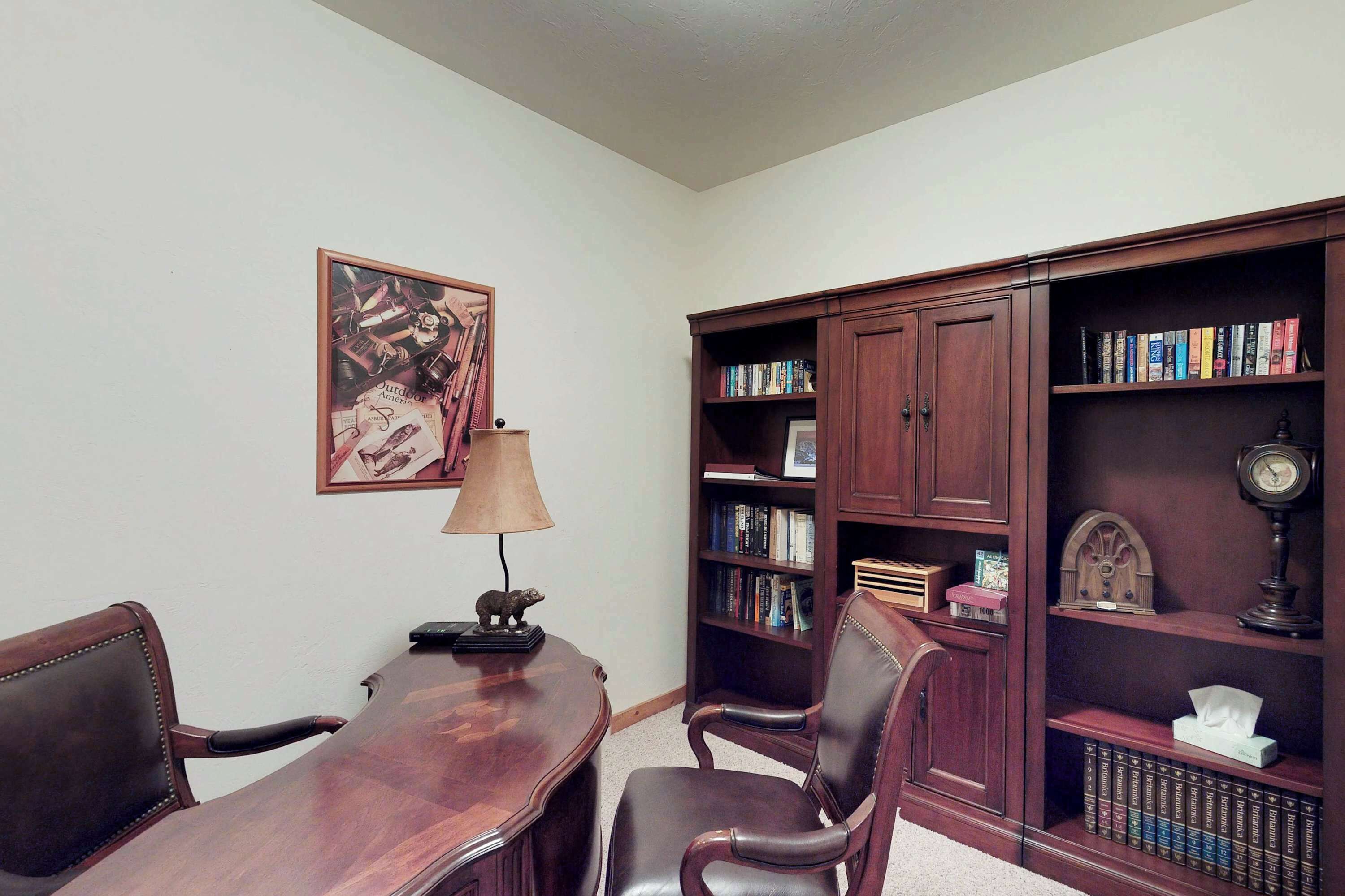 A conference room with a wooden table, two chairs, a lamp, a bookshelf, and a framed picture on the wall.
