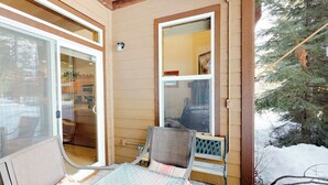 A covered porch with a sliding glass door, a small table, and two chairs. - McCall Golf Course Condo | Pools, Hot Tub & Patio (McCall)
