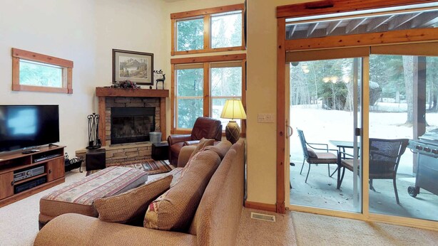 A cozy living room with a fireplace, comfortable seating, a television, and a sliding glass door leading to an outdoor patio. - McCall Golf Course Condo | Pools, Hot Tub & Patio (McCall)