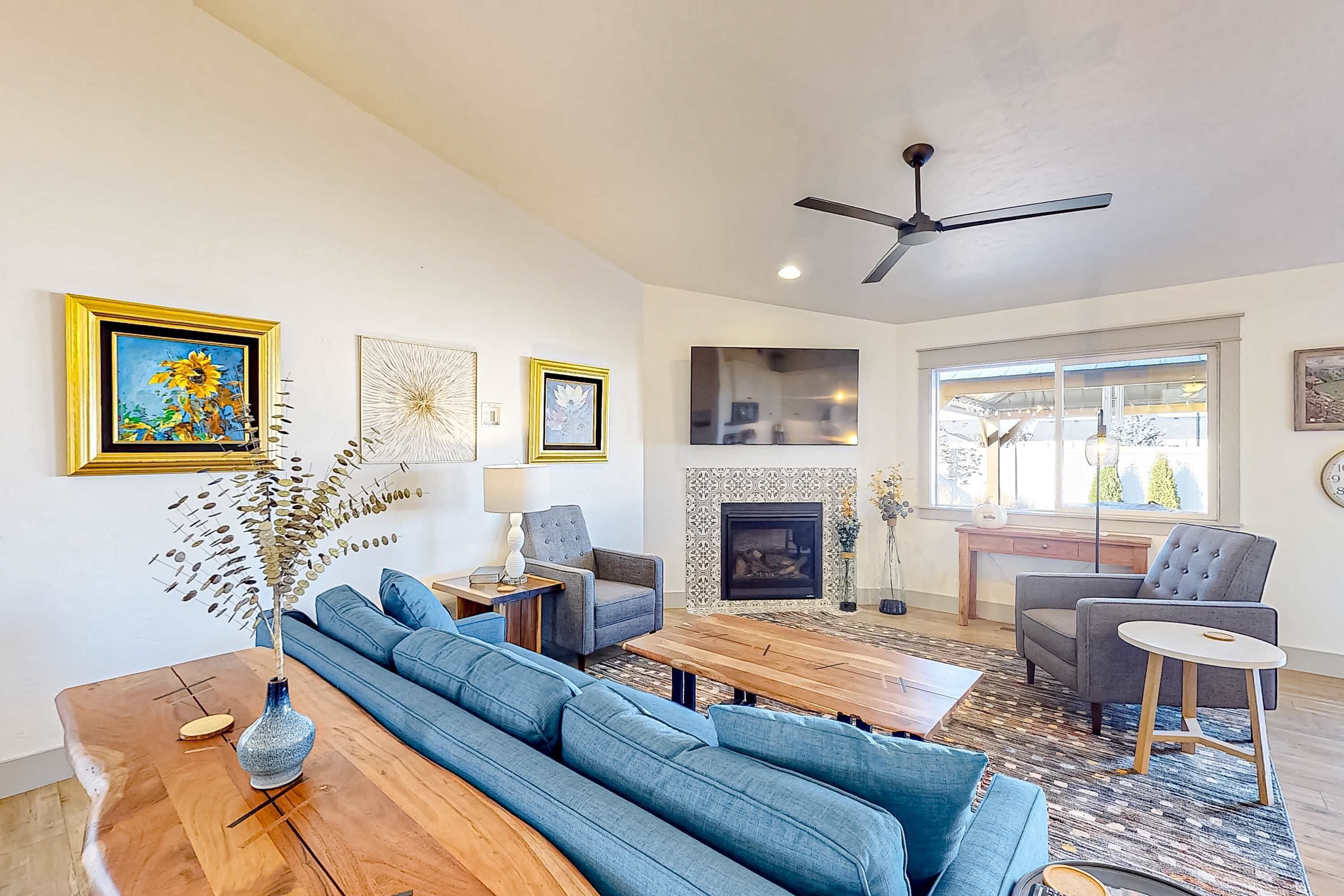 A modern living room with a sofa, coffee table, and chairs, a fireplace, and artwork on the walls.