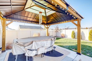 En overdækket terrasse med et bord og stole, omgivet af en træpergola og en klar himmel.