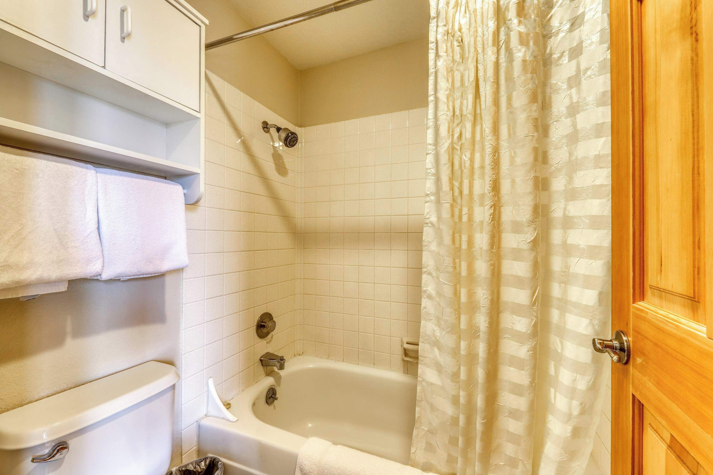 A bathroom with a white bathtub, a showerhead, a towel rack, and a wooden door.