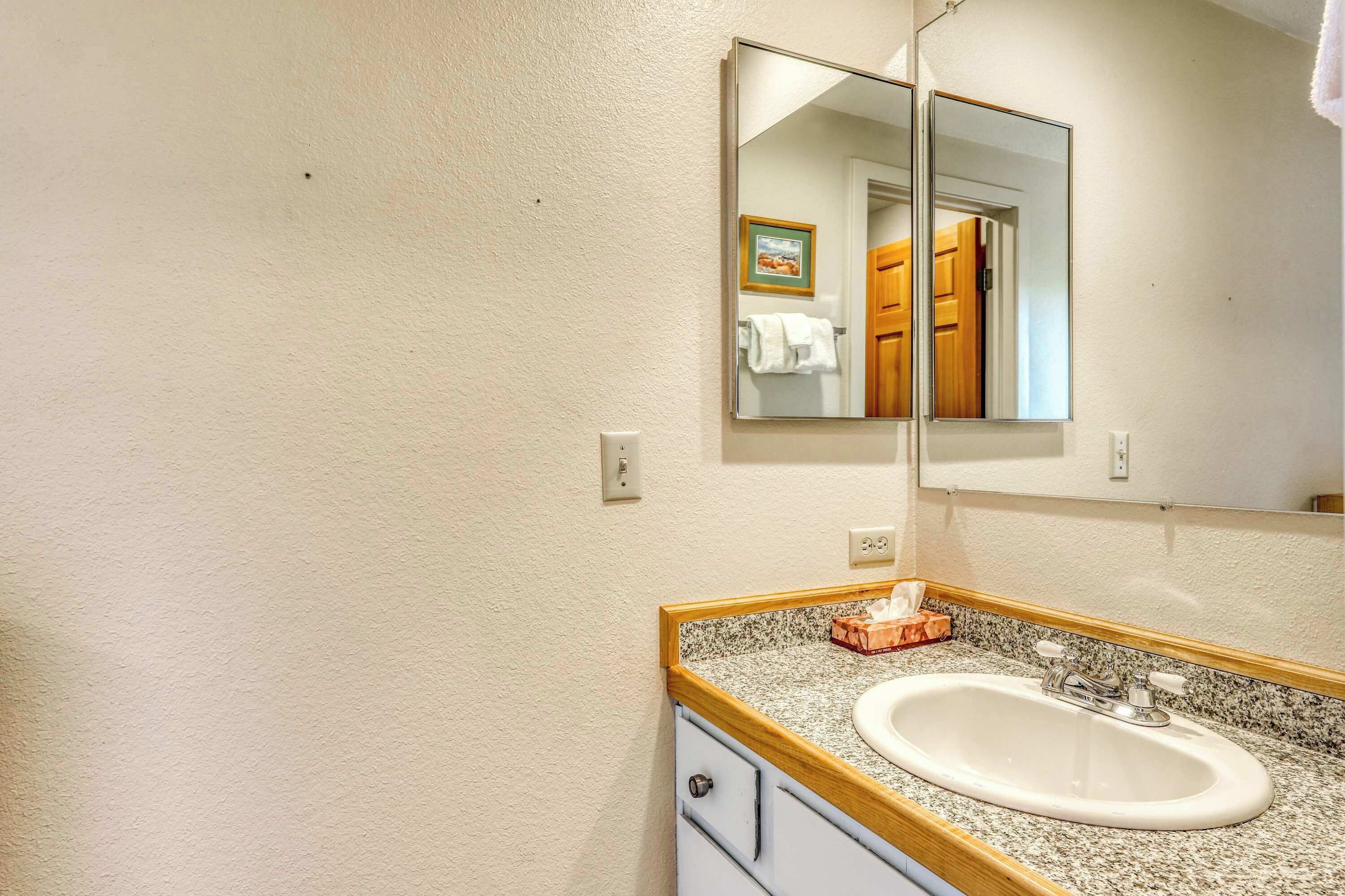 A bathroom with a white sink, a wooden vanity, a granite countertop, and a mirror.