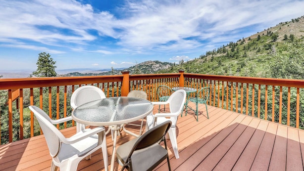 Una terraza de madera con mobiliario exterior, con vistas a un paisaje montañoso.