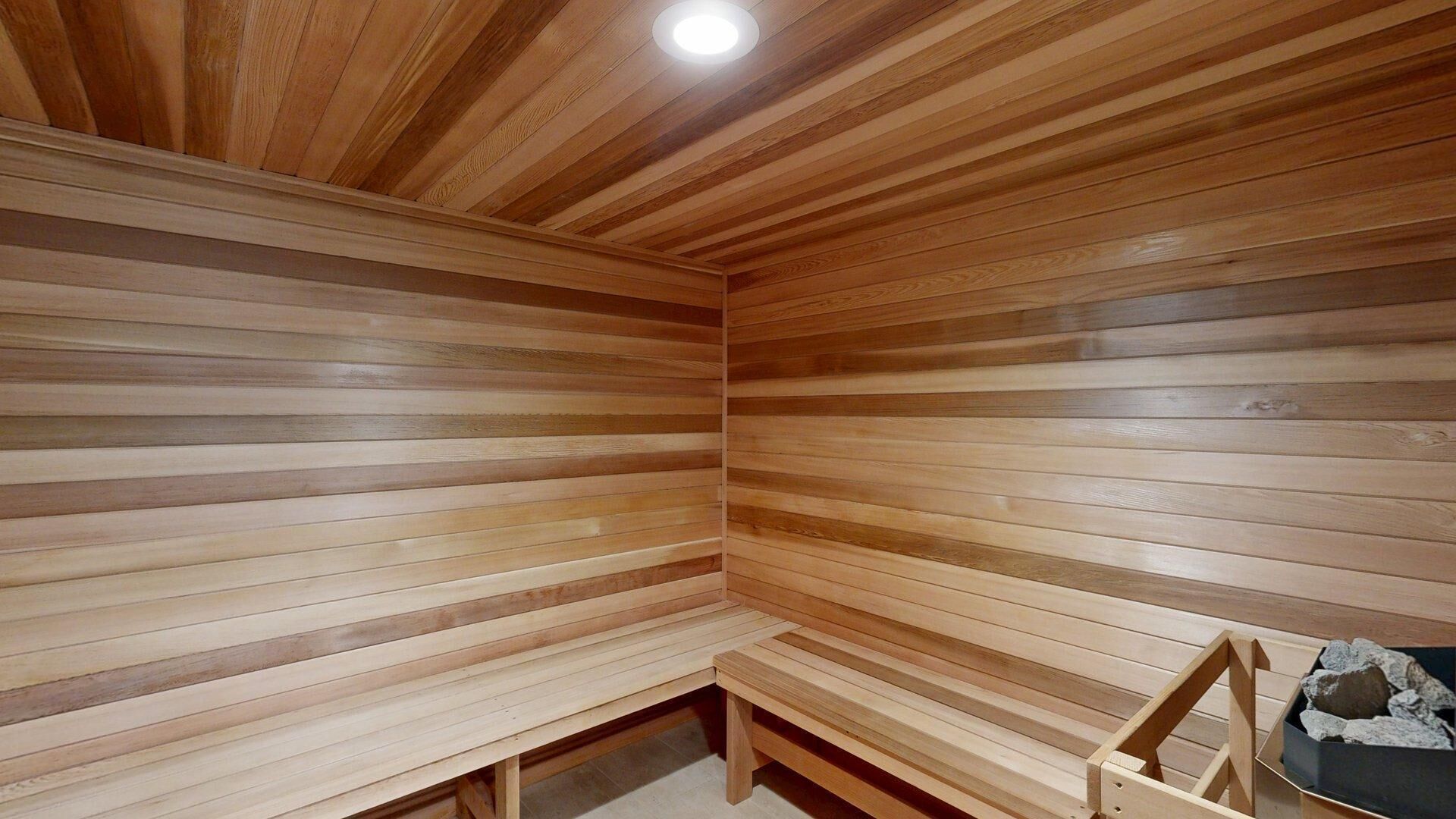 A sauna room with wooden slats on the walls and ceiling, a bench, and a small table with rocks.