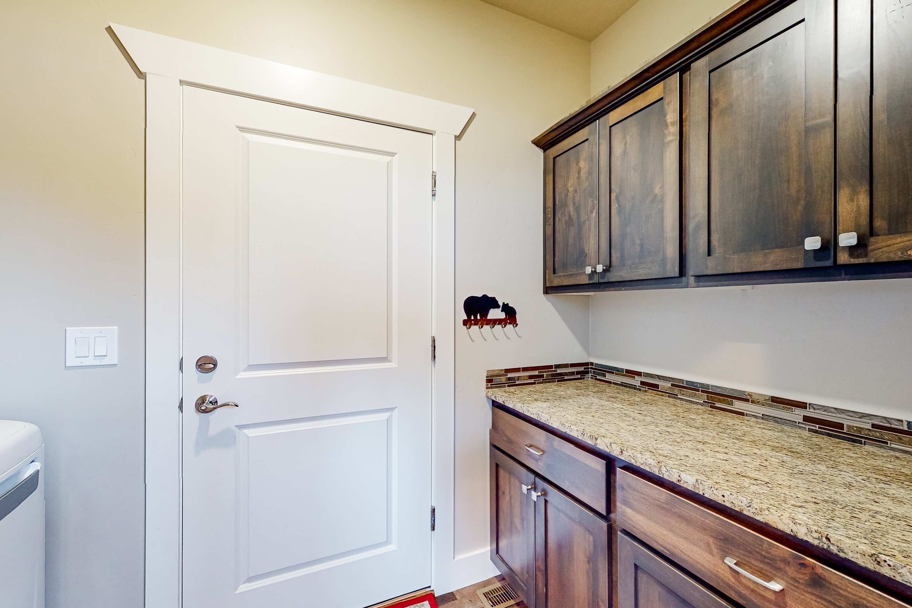 A kitchen with a white door, dark wooden cabinets, and a granite countertop.