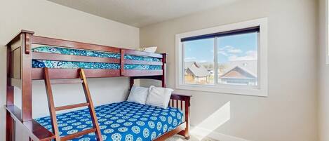 A bunk bed with a ladder, a window with a view of houses, and a carpeted floor.
