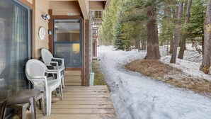 Een houten terras met stoelen, een deur en uitzicht op een besneeuwd bos.