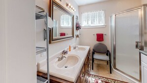 Een badkamer met een dubbele wastafel, een spiegel, een douche en een stoel.