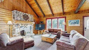 A log cabin interior with a stone fireplace, leather sofas, a television, and a stone wall.