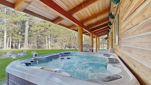 Un jacuzzi bajo una pérgola de madera con vistas a una zona boscosa.