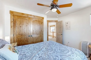 Une chambre avec un grand lit, une armoire en bois, un ventilateur de plafond et un radiateur.