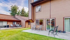 Una casa de dos pisos con un patio que incluye mobiliario exterior y césped.