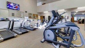 Un gimnasio con cintas de correr, elípticas y un televisor en la pared.