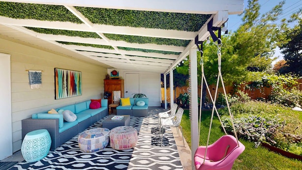 Une terrasse couverte avec un sol à motifs, un ensemble de canapés et une chaise suspendue.