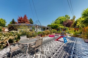 A patio with a patterned floor, outdoor furniture, and a swing set. - Family Friendly Boise Home Patio & Yard (Boise)