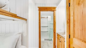 A bedroom with a bunk bed, wooden wardrobe, and a bathroom with a glass shower.