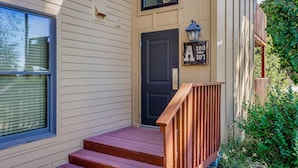 A beige house with a black front door, a wooden staircase, and a small porch area.