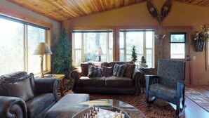 A cozy living room with a wooden ceiling, a leather sofa, a patterned armchair, and a chess table. - New Meadows Cabin Game Room, Pool & Deck (New Meadows)