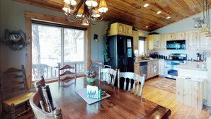 A wooden dining table with chairs, a chandelier, and a view of the outdoors. - New Meadows Cabin Game Room, Pool & Deck (New Meadows)