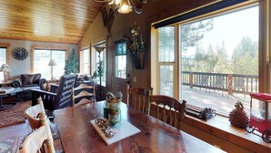 A wooden interior with a dining table, chairs, and a large window overlooking a deck. - New Meadows Cabin Game Room, Pool & Deck (New Meadows)