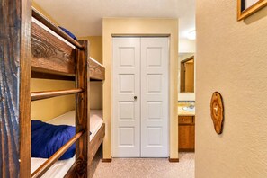 Una habitación con literas, una puerta blanca, un baño con lavamanos y espejo, y una decoración de pared de madera.