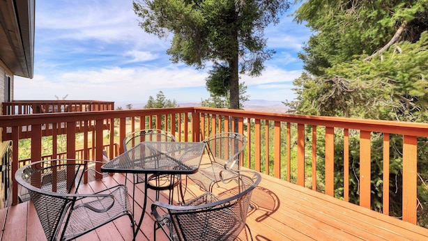 A wooden deck with metal chairs and a table, overlooking a forested area.