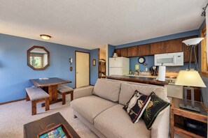 Un espacio habitable compacto con kitchenette, comedor y sofá con cojín decorativo.