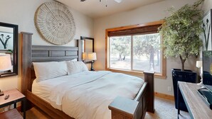 Ein Schlafzimmer mit Bett, Deckenventilator, großem Fenster, Pflanze und Schreibtisch mit Lampe.