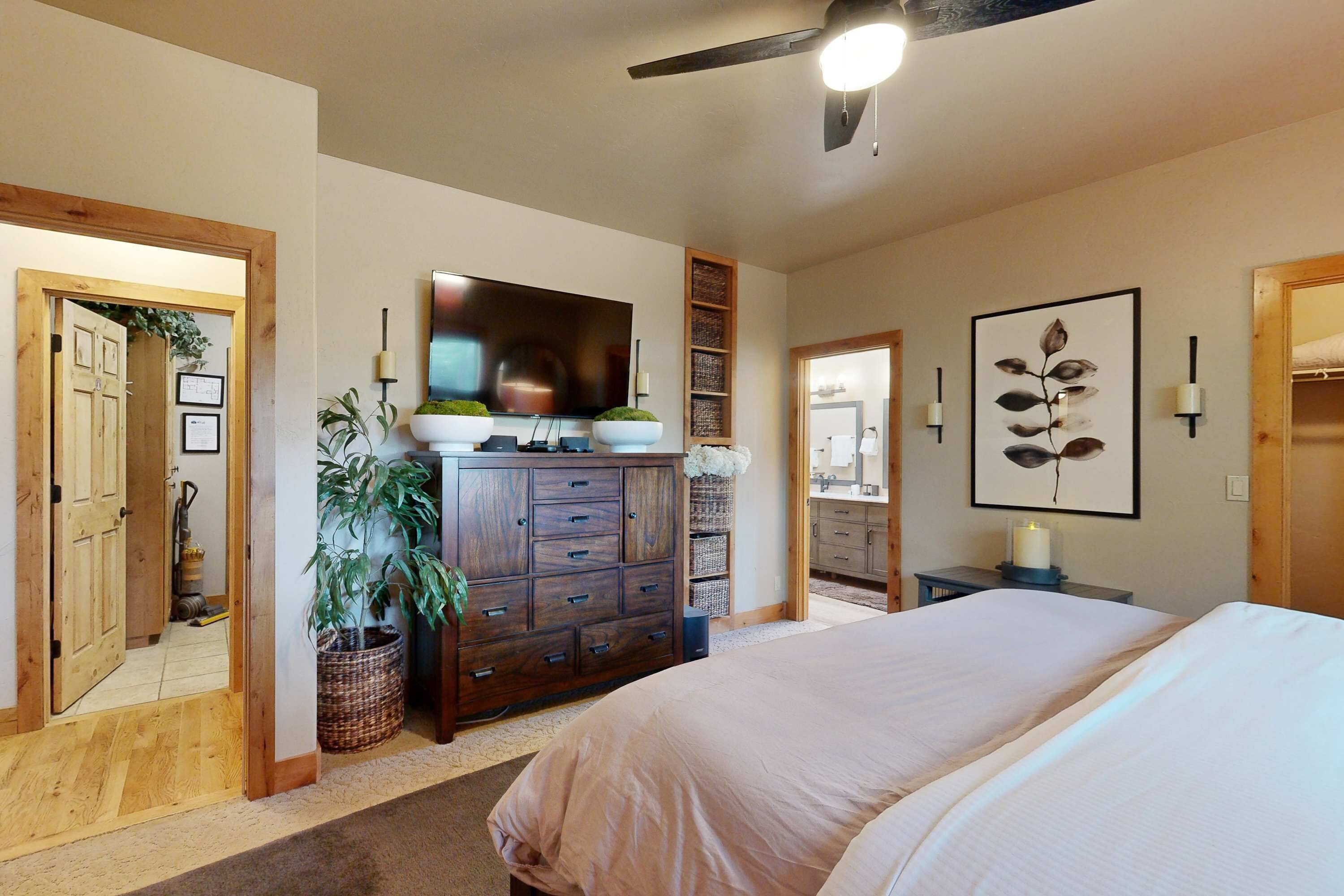 A bedroom with a large bed, a dresser, a television, and a ceiling fan.