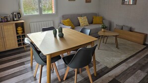 Ein modernes Wohnzimmer mit einem Holzespeisetisch, zwei schwarzen Stühlen, einem grauen Sofa mit gelben Kissen und einem kleinen runden Tisch mit einer Pflanze.