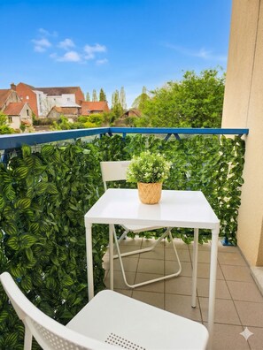 A balcony with a white table and chair, a potted plant, and a view of houses and trees. - Arras city stay - parking - balcony (Arras)