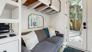 A modern living room with a grey sofa, a mirror, and a door leading to an outdoor area. - Charming Tiny Home in Boise's North End (Boise)