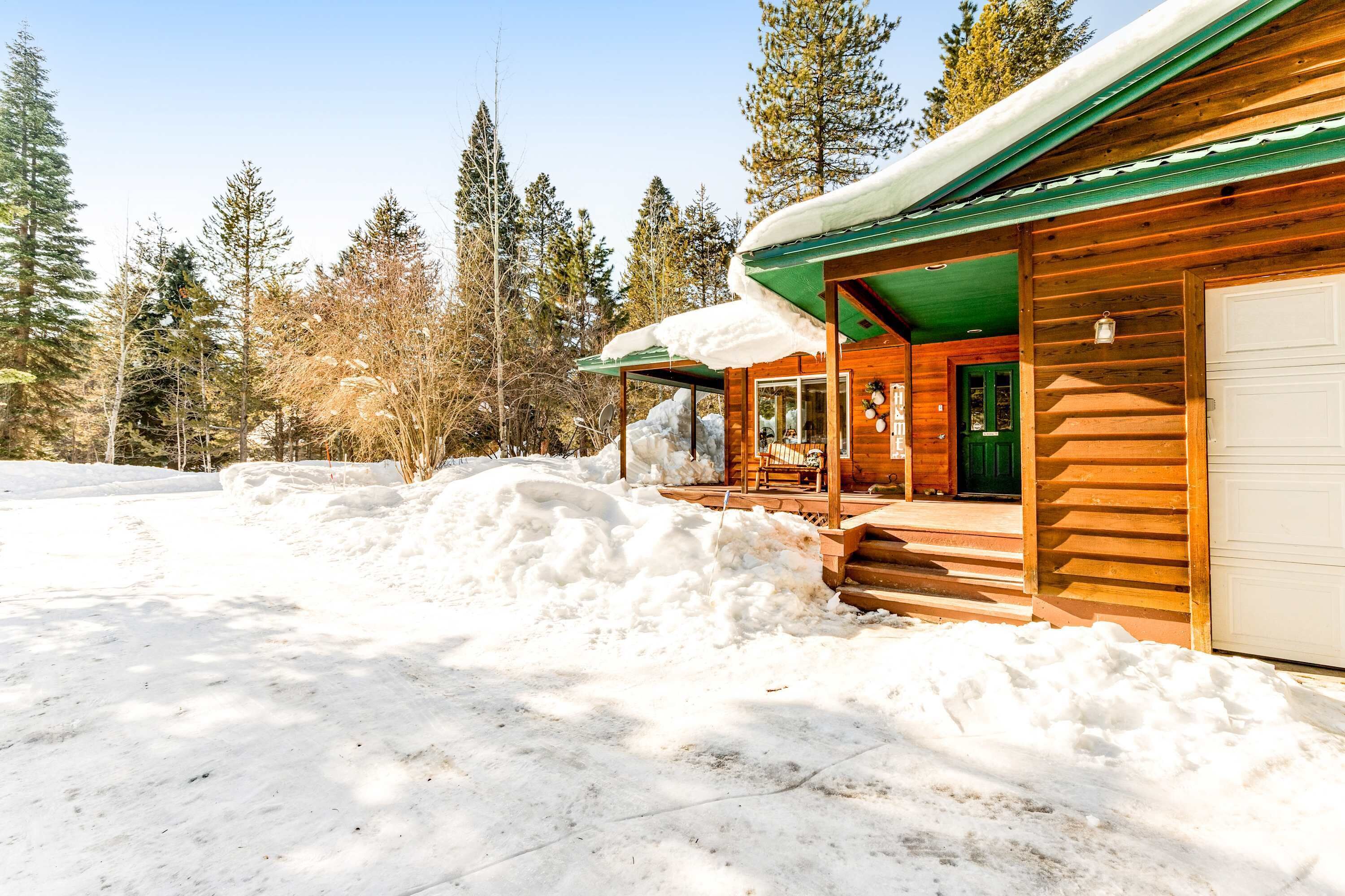 Una cabaña de madera con un porche cubierto, un garaje y un paisaje cubierto de nieve.