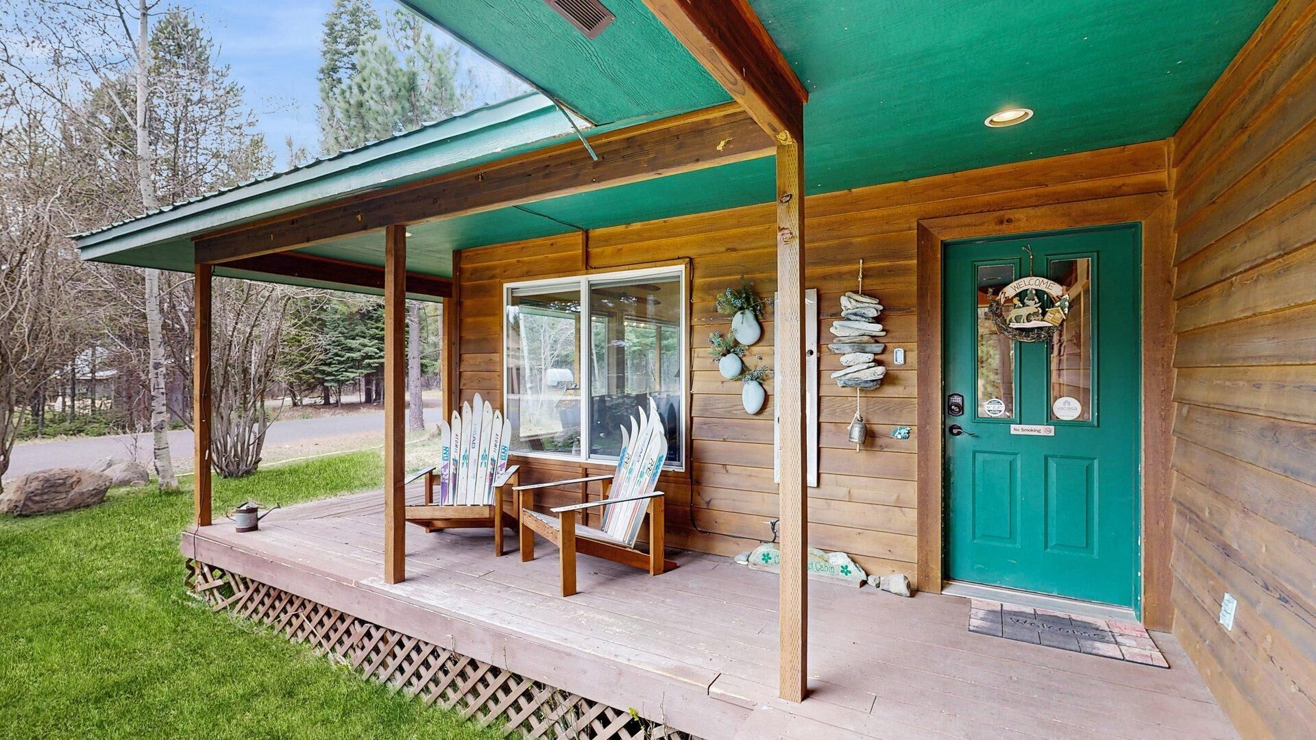 Une cabane en bois avec un porche, une porte verte et une pancarte indiquant « Bienvenue ».