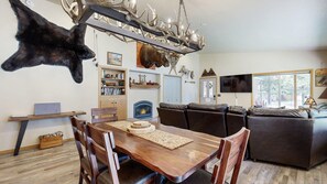 A dining area with a wooden table and chairs, a fireplace, and a mounted animal head. - McCall Family Retreat Near Payette Lake | Hot Tub (McCall)