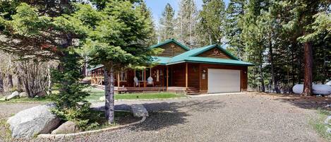 A lodge with a covered porch, a garage, and a gravel driveway surrounded by trees.