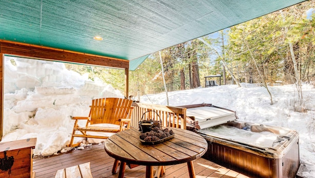 A wooden deck with a hot tub, wooden chairs, and a table with a basket of pine cones. - McCall Family Retreat Near Payette Lake | Hot Tub (McCall)