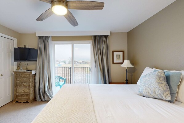 A hotel room with a bed, a ceiling fan, a TV, a dresser, a balcony with curtains, and a window. - Private Townhome - Mountain Views & 2 Baths (Boise)