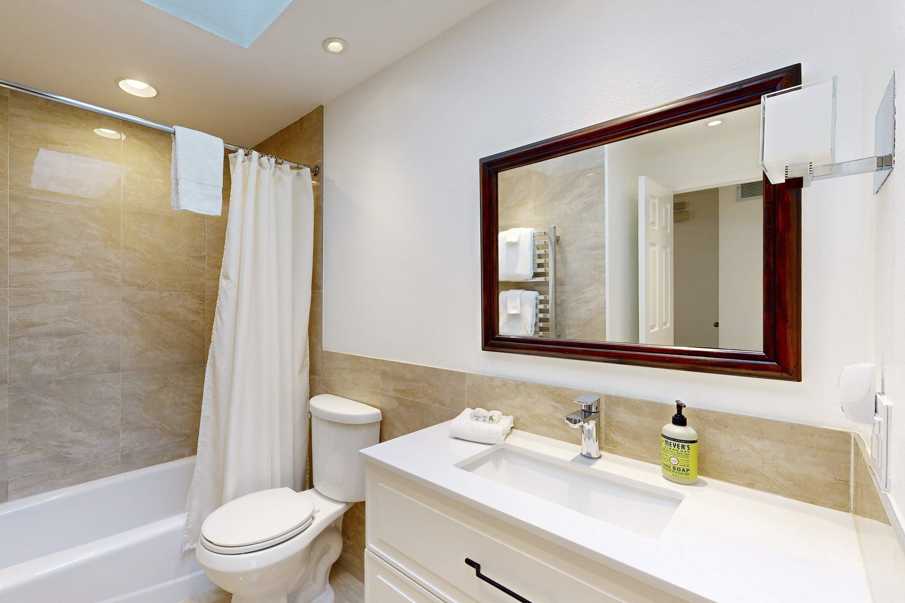 A bathroom with a bathtub, toilet, vanity with a mirror, and a bottle of hand soap.